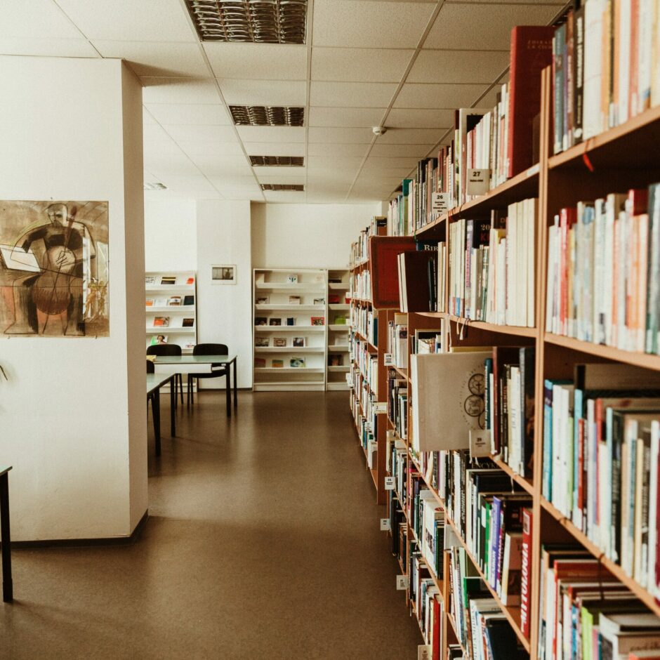 Bibliotēkas telpas, kur labajā pusē ir grāmatas un kreisajā galdi lasīšanai